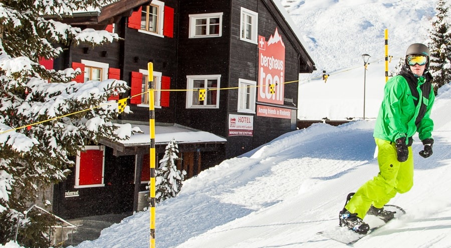 Snowboardfahrer auf der Piste neben dem Berghaus Toni