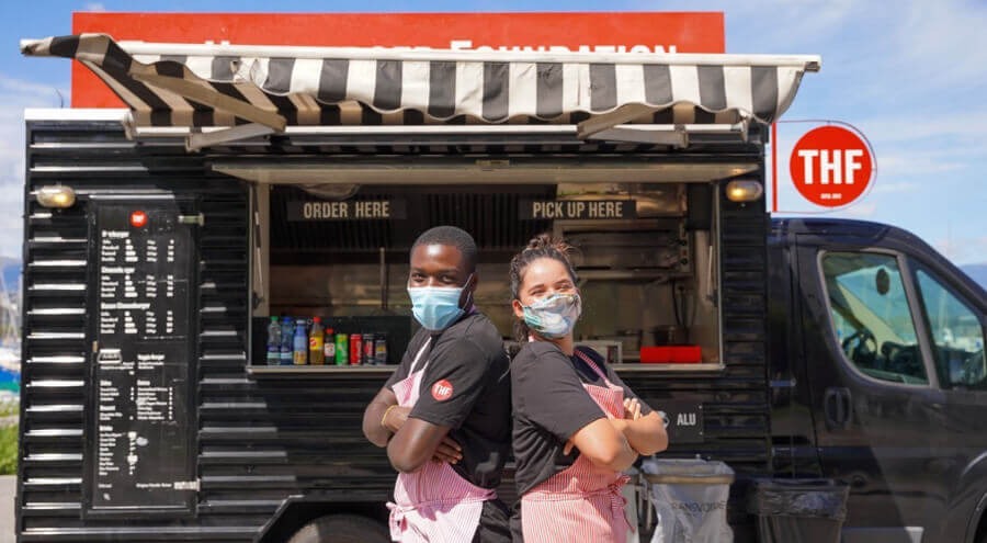 Mitarbeiter in Maske vor einem Foodtruck der Hamburger Foundation