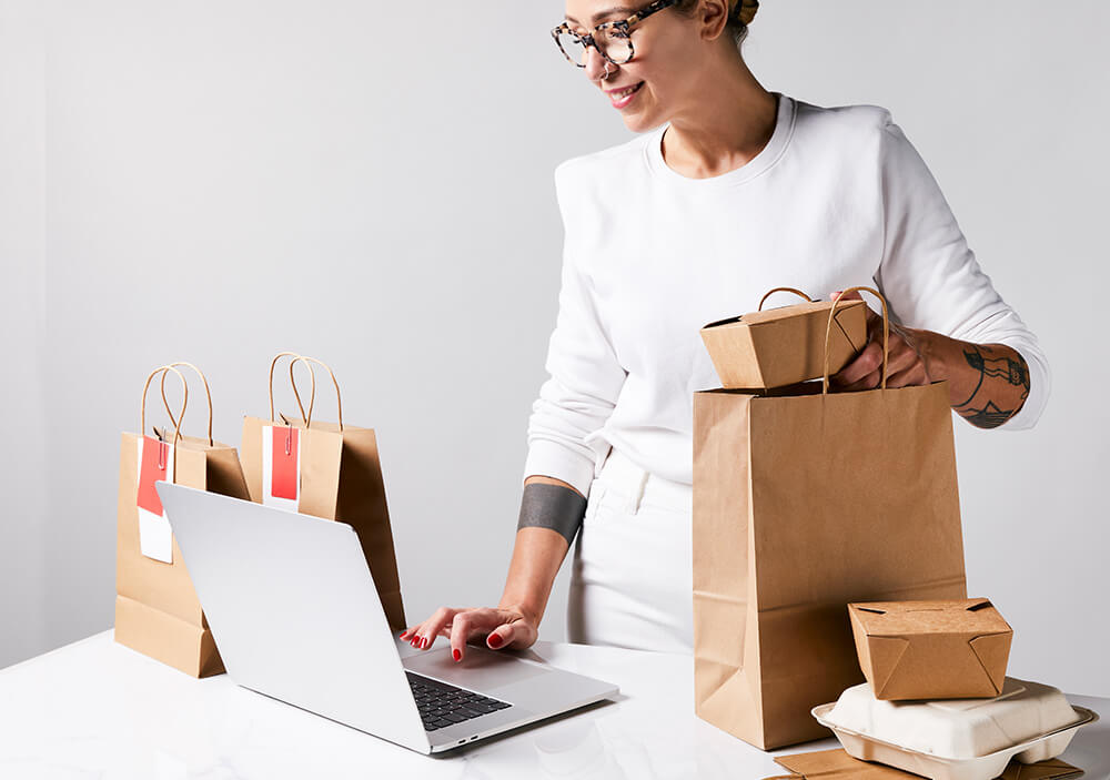 Frau bedient Laptop mit diversen Liefergerichten auf dem Tisch